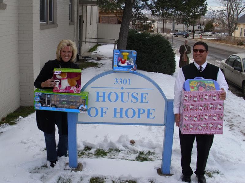 Two people from the practice holding donated toys beside the House of Hope sign in the snow.